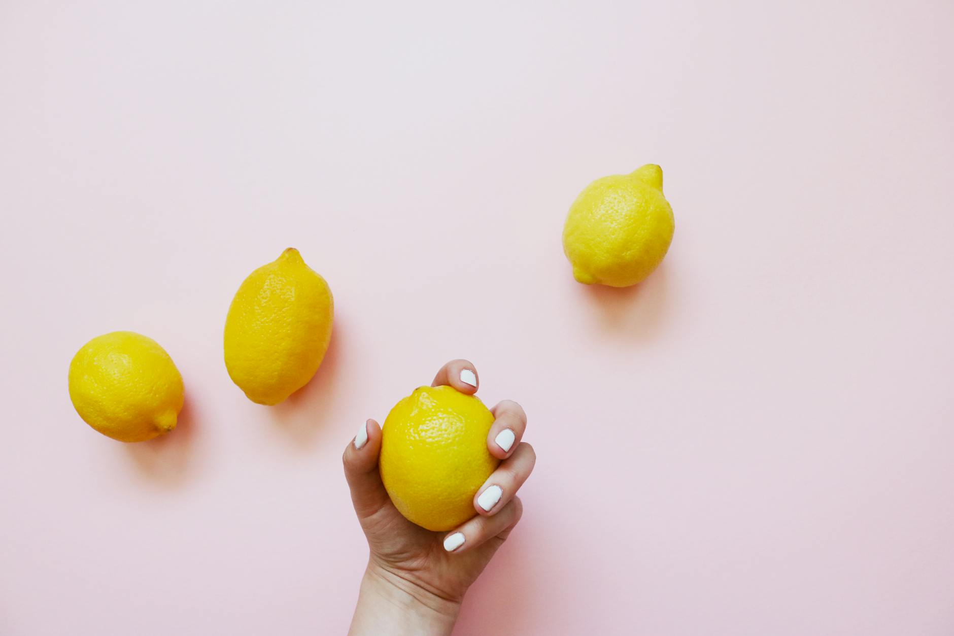 A hand holding a fresh lemon on a pink background, symbolizing pleasure and vitality.