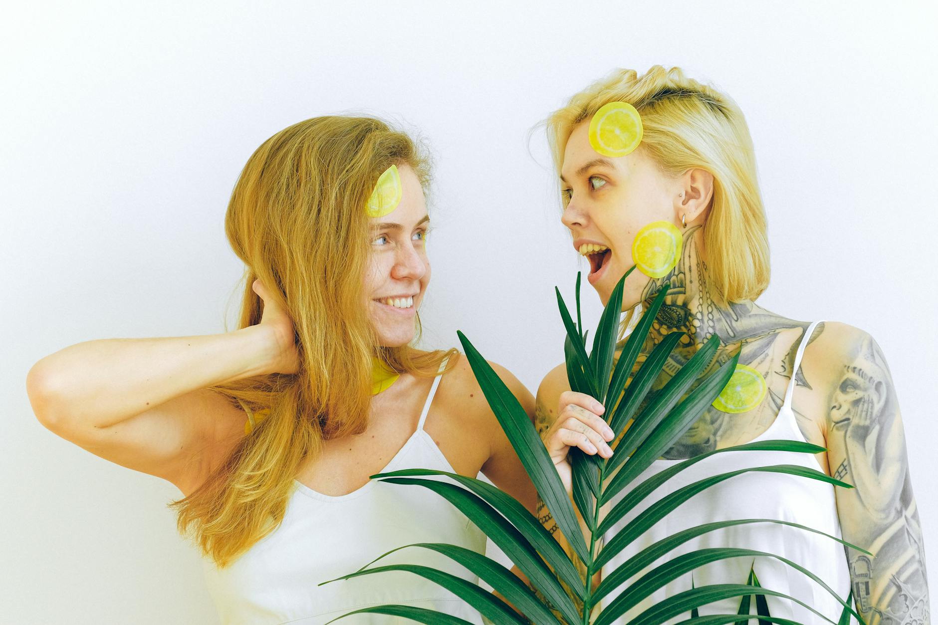 Two women smiling with lemon slices and tropical plants, expressing joy and ease indoors