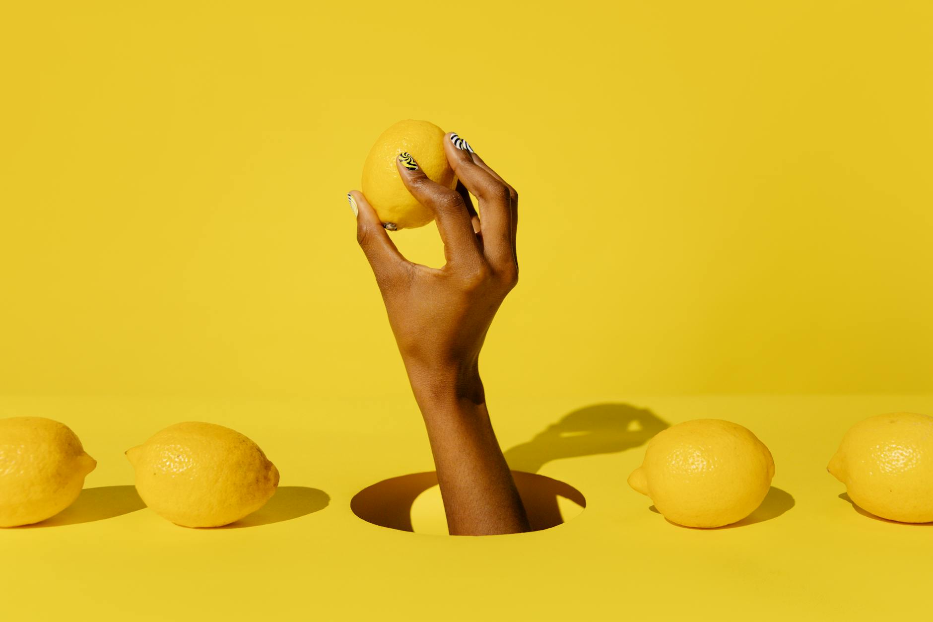 A hand holding a fresh lemon against a bright yellow background, symbolizing the vibrant clarity lemon vibrators bring to pleasure