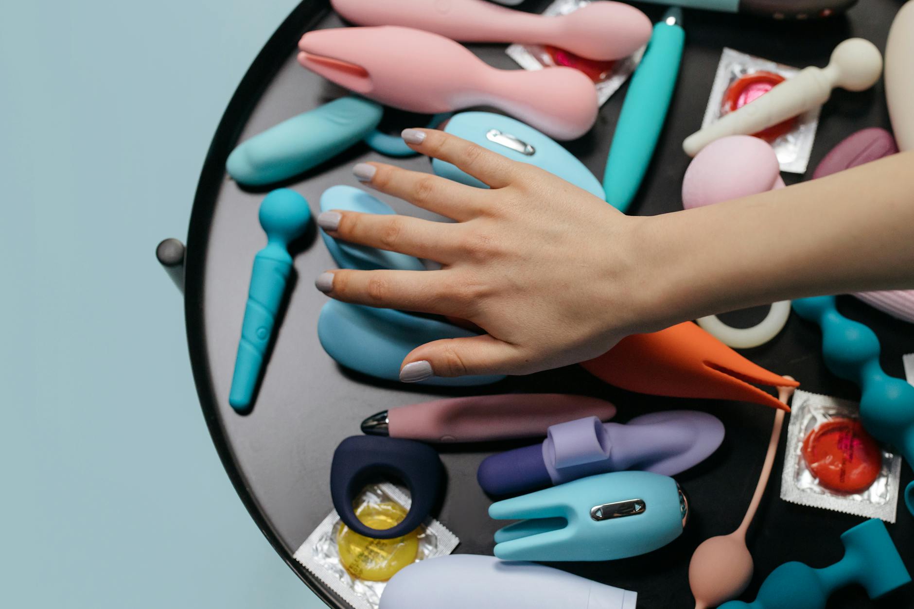 Two hands holding pink and blue clitoral vibrators against a pastel background