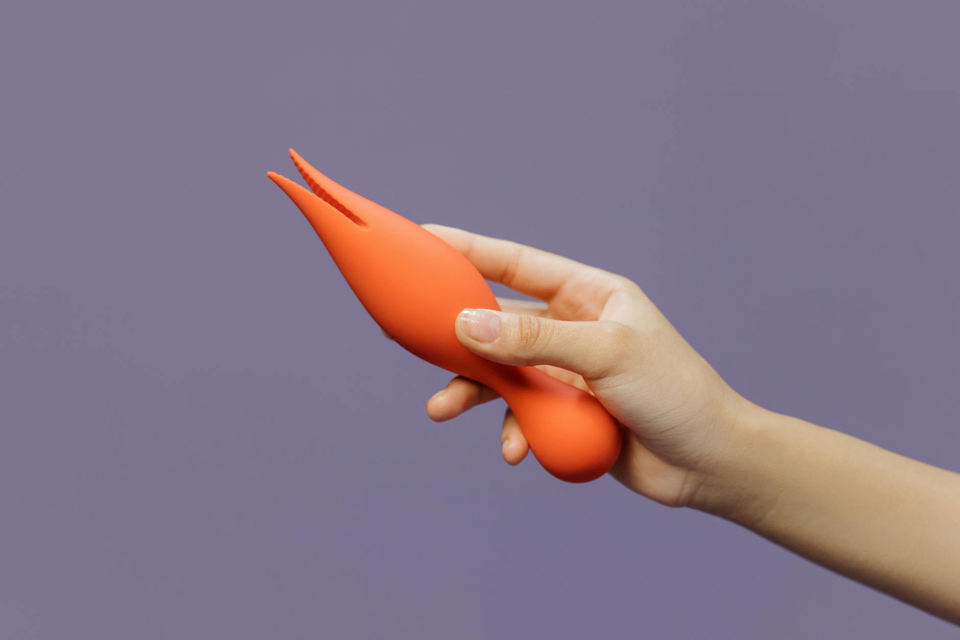 A hand holding a lemon-colored vibrator against a minimalist backdrop, highlighting its distinctive shape and design.